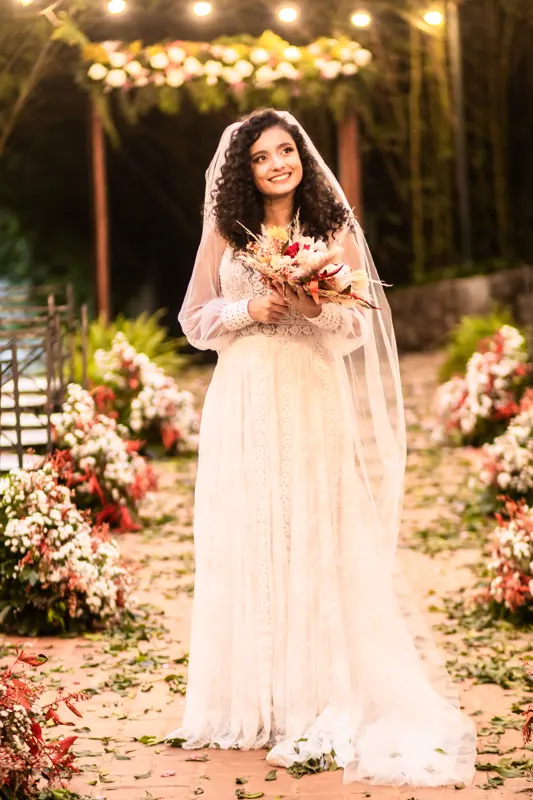 Noiva de cabelos cacheados sorrindo com o buquê no altar