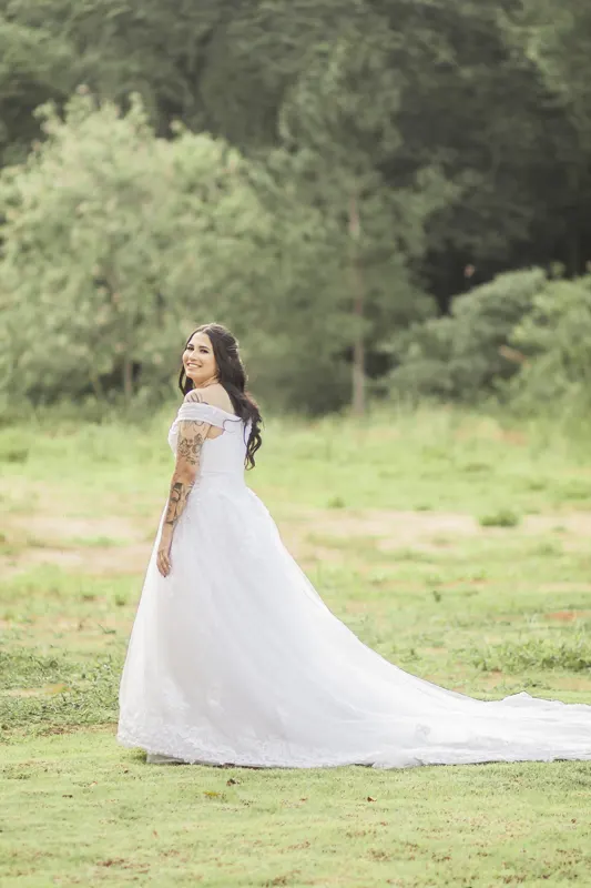 Noiva tatuada olhando por cima do ombro com a cauda do vestido no gramado
