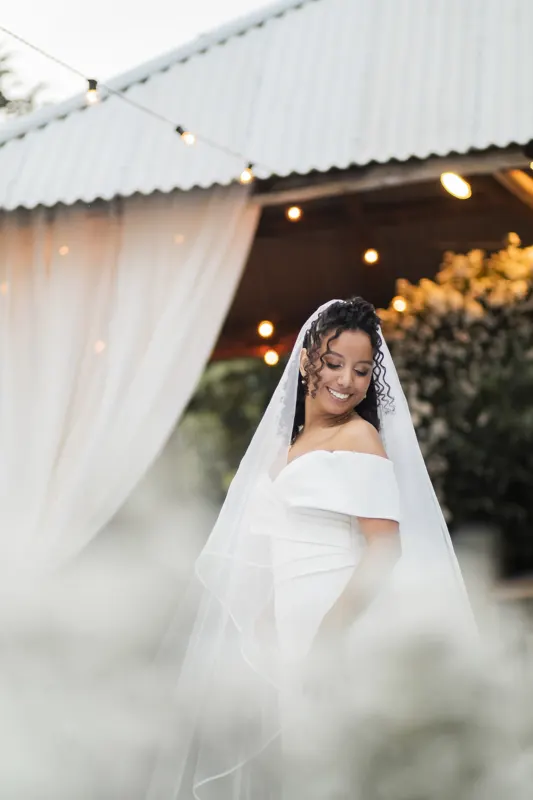 Noiva sorrindo com o véu entre cortinas e luzes