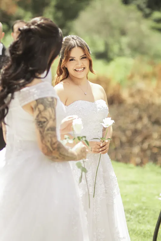 Noiva sorrindo segurando uma rosa branca na cerimônia