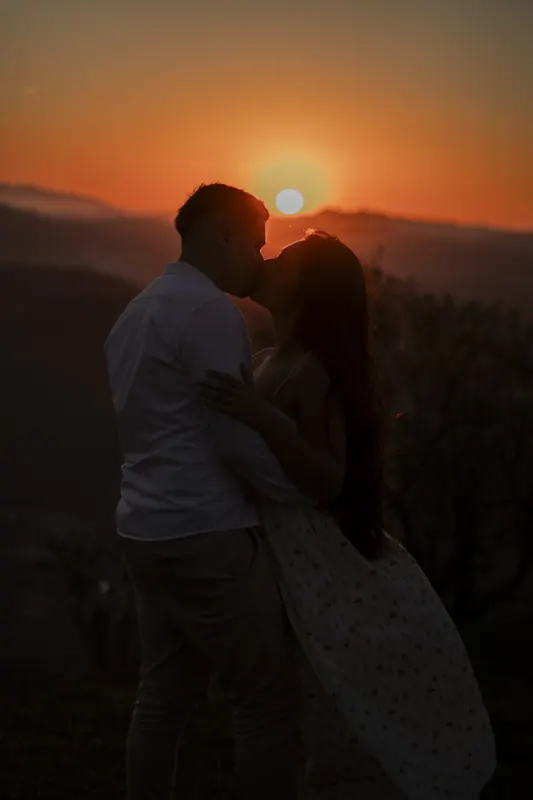 Beijo do casal em silhueta com o sol encostando na serra