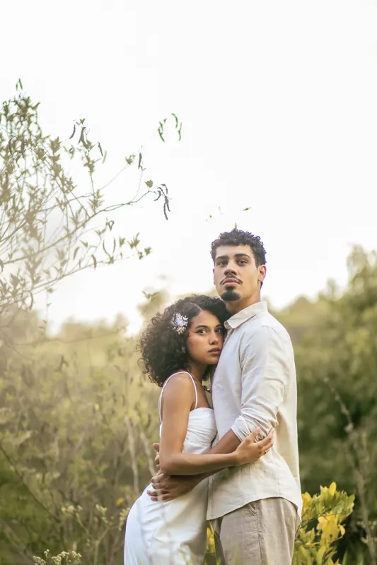 Casal abraçado em meio ao mato alto olhando para a câmera