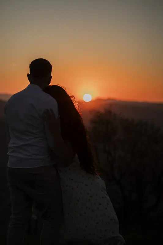 Casal abraçado de costas vendo o sol se pôr