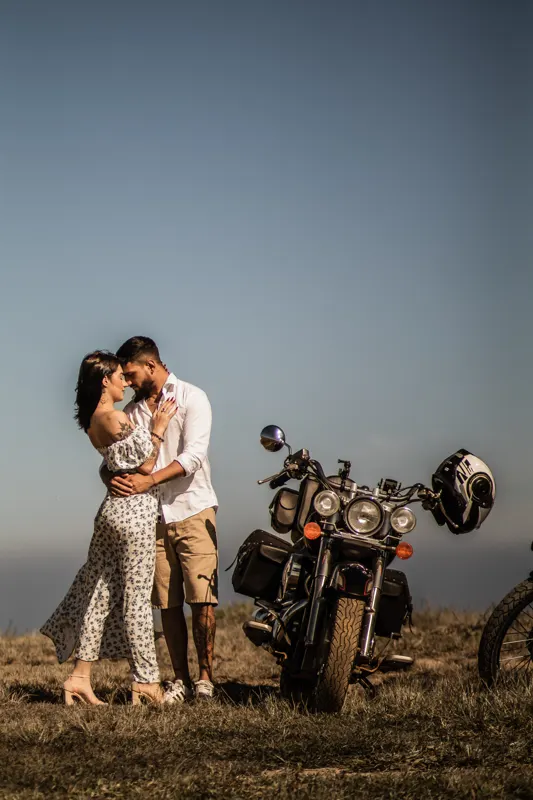 Casal abraçado ao lado de uma moto no alto do morro