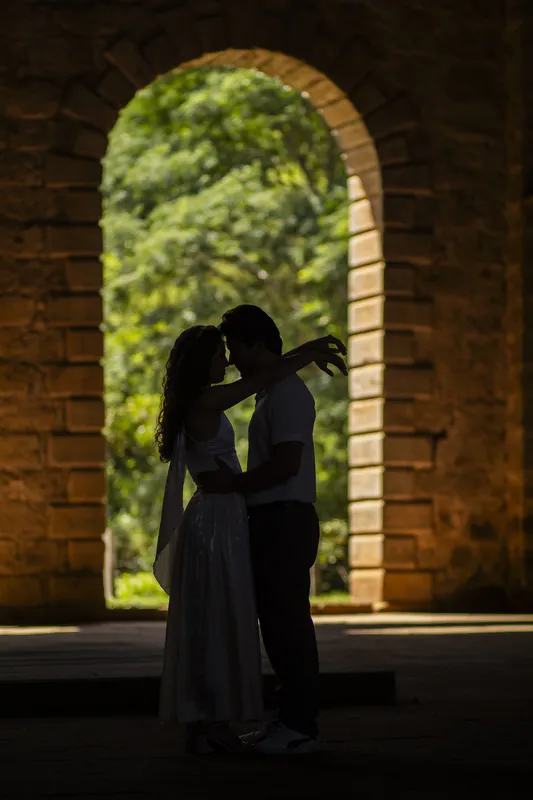 Silhueta do casal se abraçando sob um arco de pedra