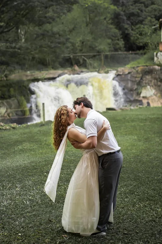 Beijo do casal no gramado em frente a uma cachoeira