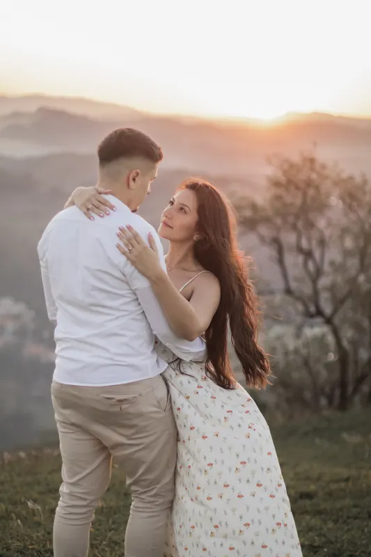 Casal abraçado olhando um para o outro com o pôr do sol na serra