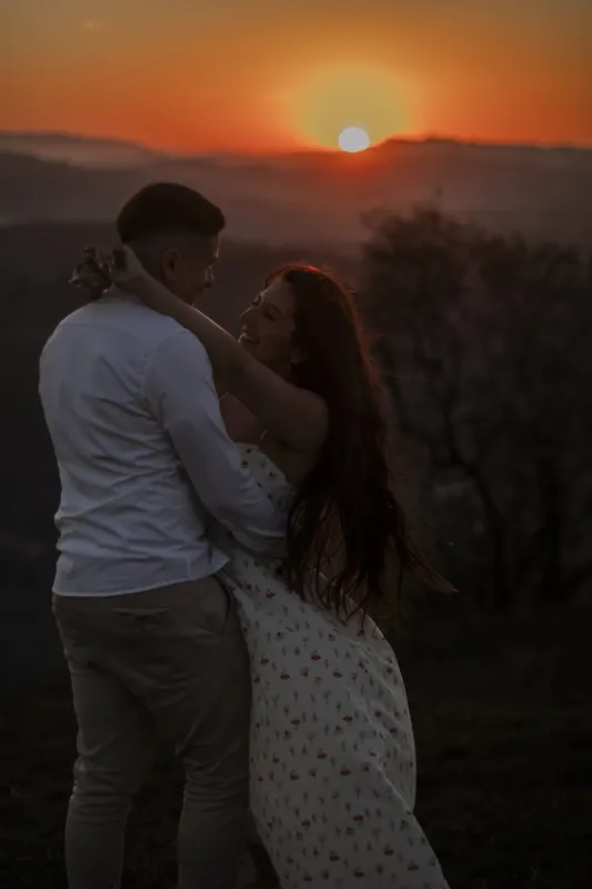 Casal rindo abraçado contra o sol se pondo