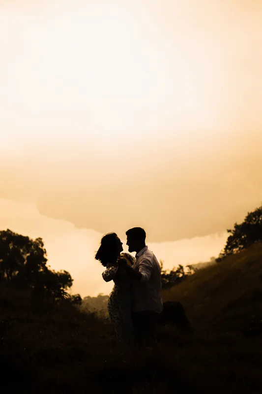 Silhueta do casal dançando no morro com o céu dourado