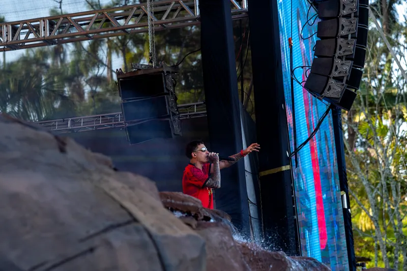 Cantor estendendo o braço para o público atrás das pedras do palco